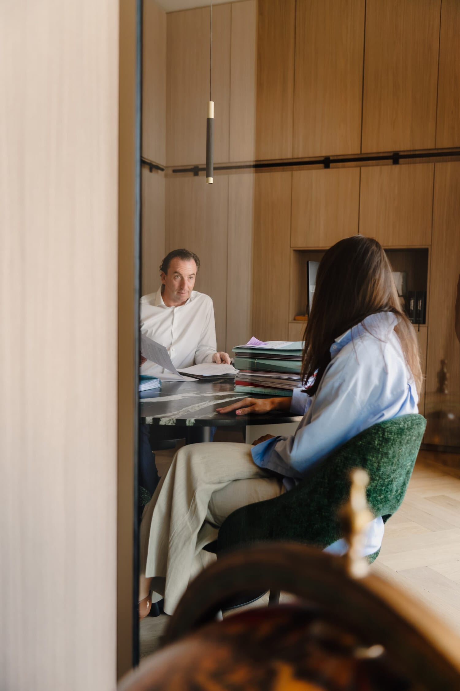 Twee personen zitten aan een tafel in een moderne, lichte ruimte met houten panelen, bezig met papierwerk.