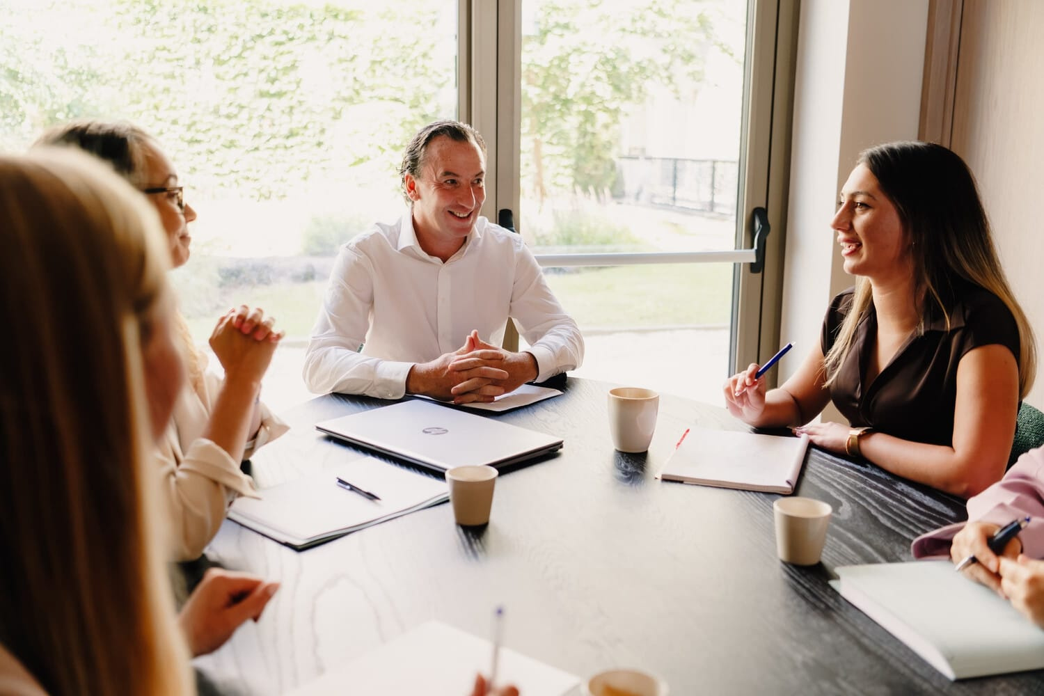Een groep mensen zit rond een tafel in een vergaderzaal en bespreekt informatie, met notitieblokken en koffiekopjes.